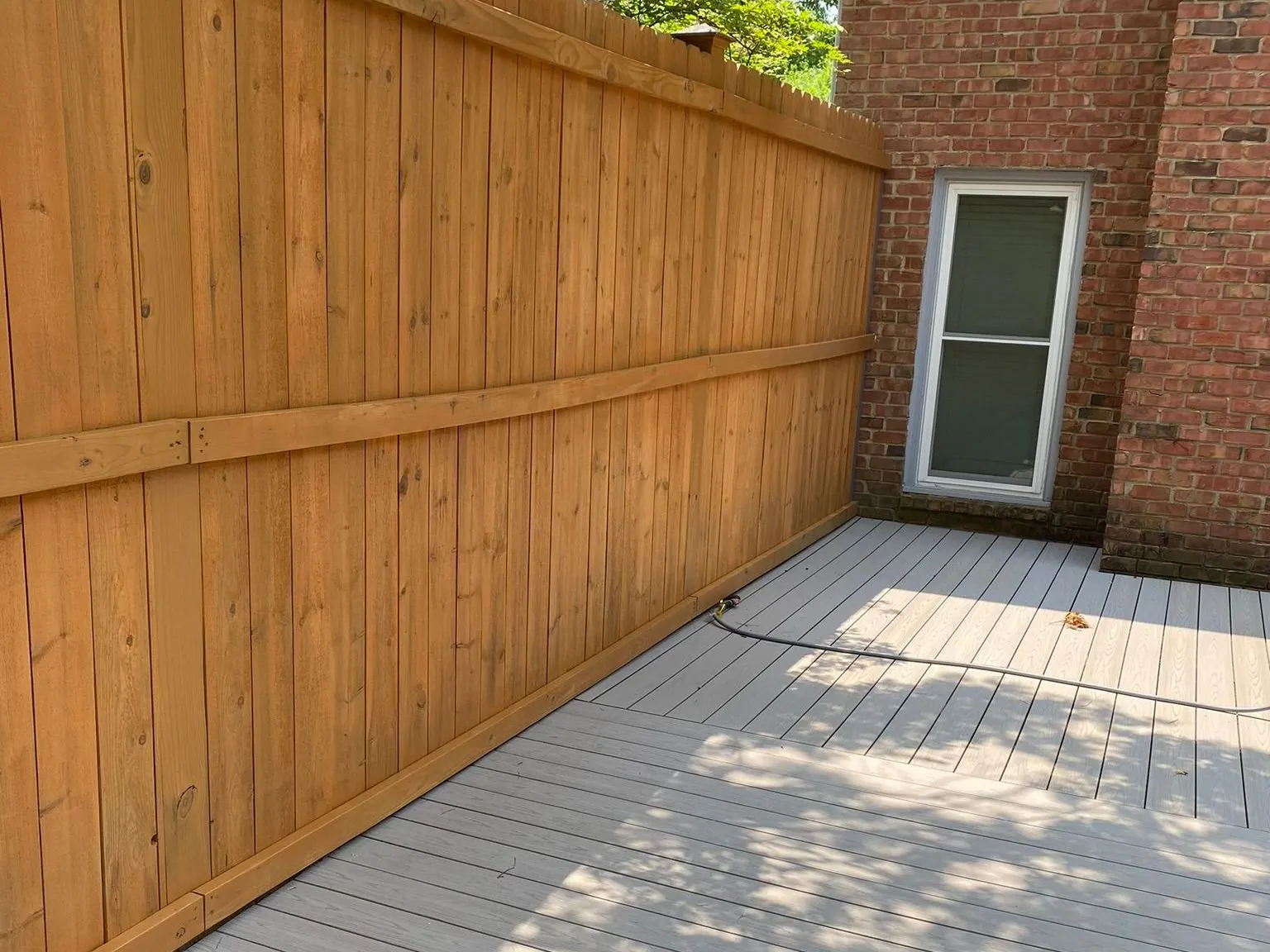 Cedar-stained privacy fence running along a gray deck beside a brick house, one of our fence staining projects for Bellevue homes